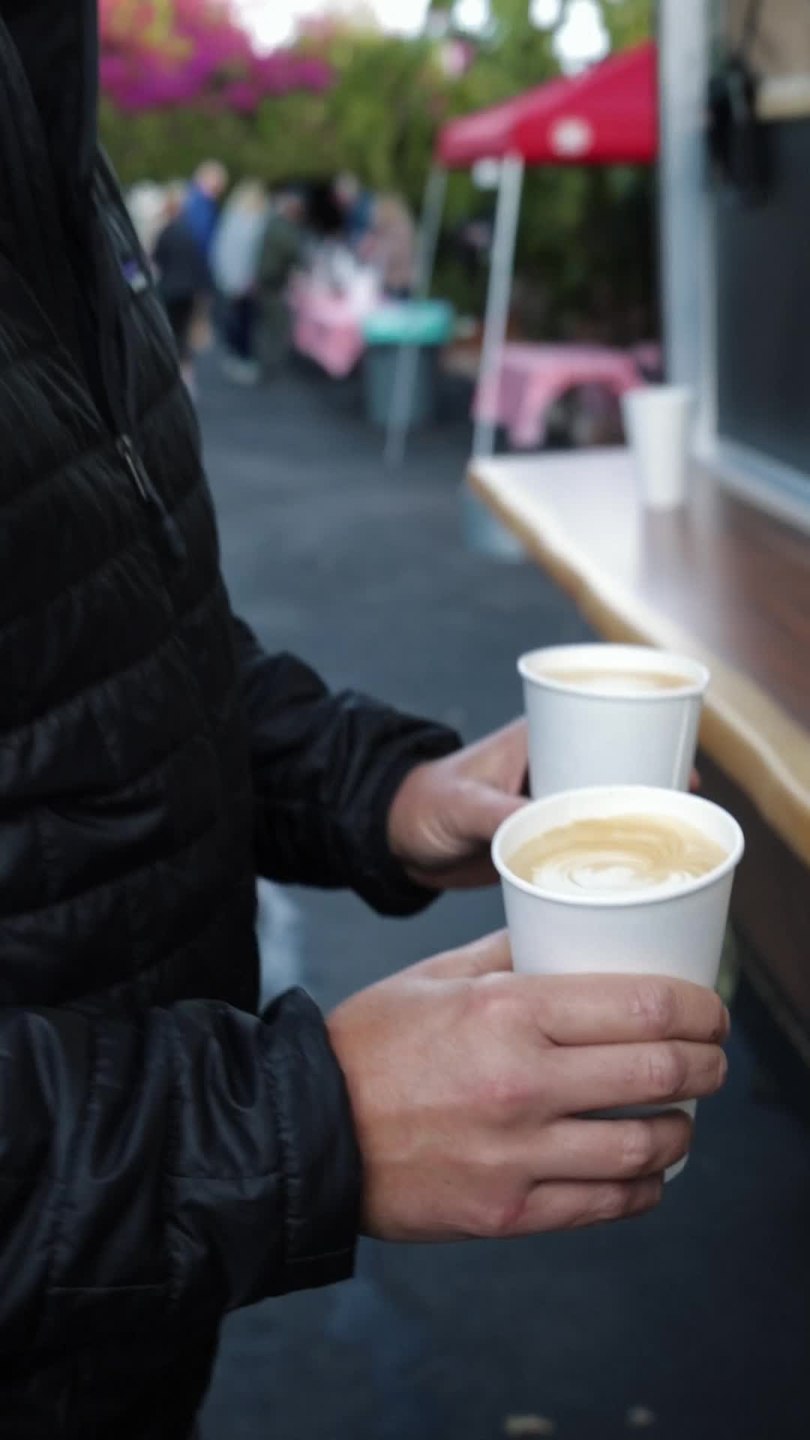 Customer hands holding two cups of coffee beside the truck