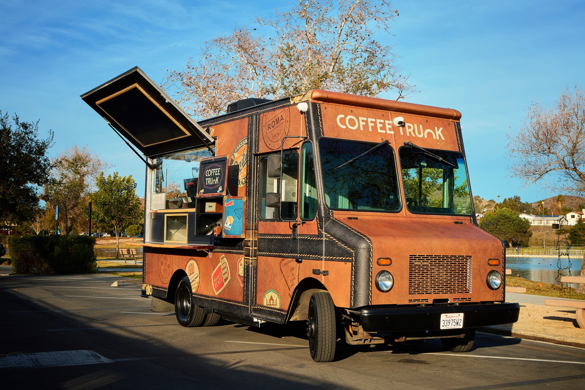 Three-quarter view of the small brown Coffee Trunk parked beside a lake, service hatch open